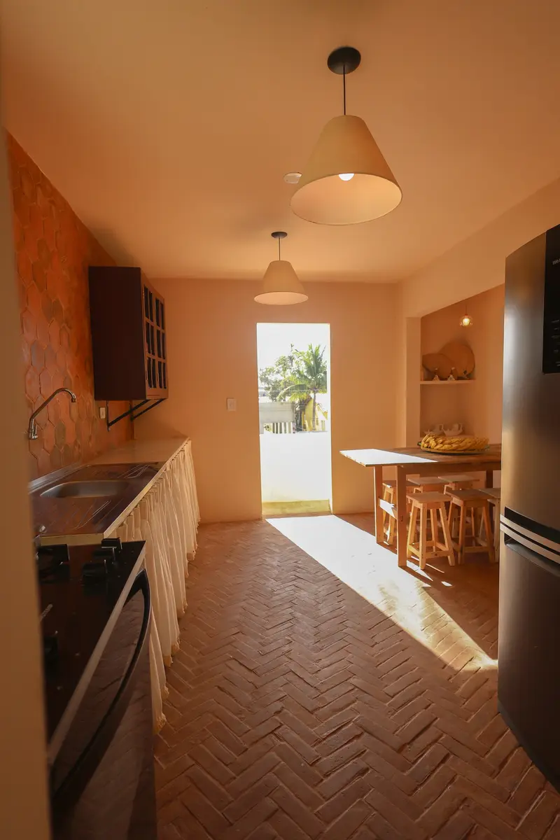 Cozinha com piso de tijolinho e porta aberta para o quintal