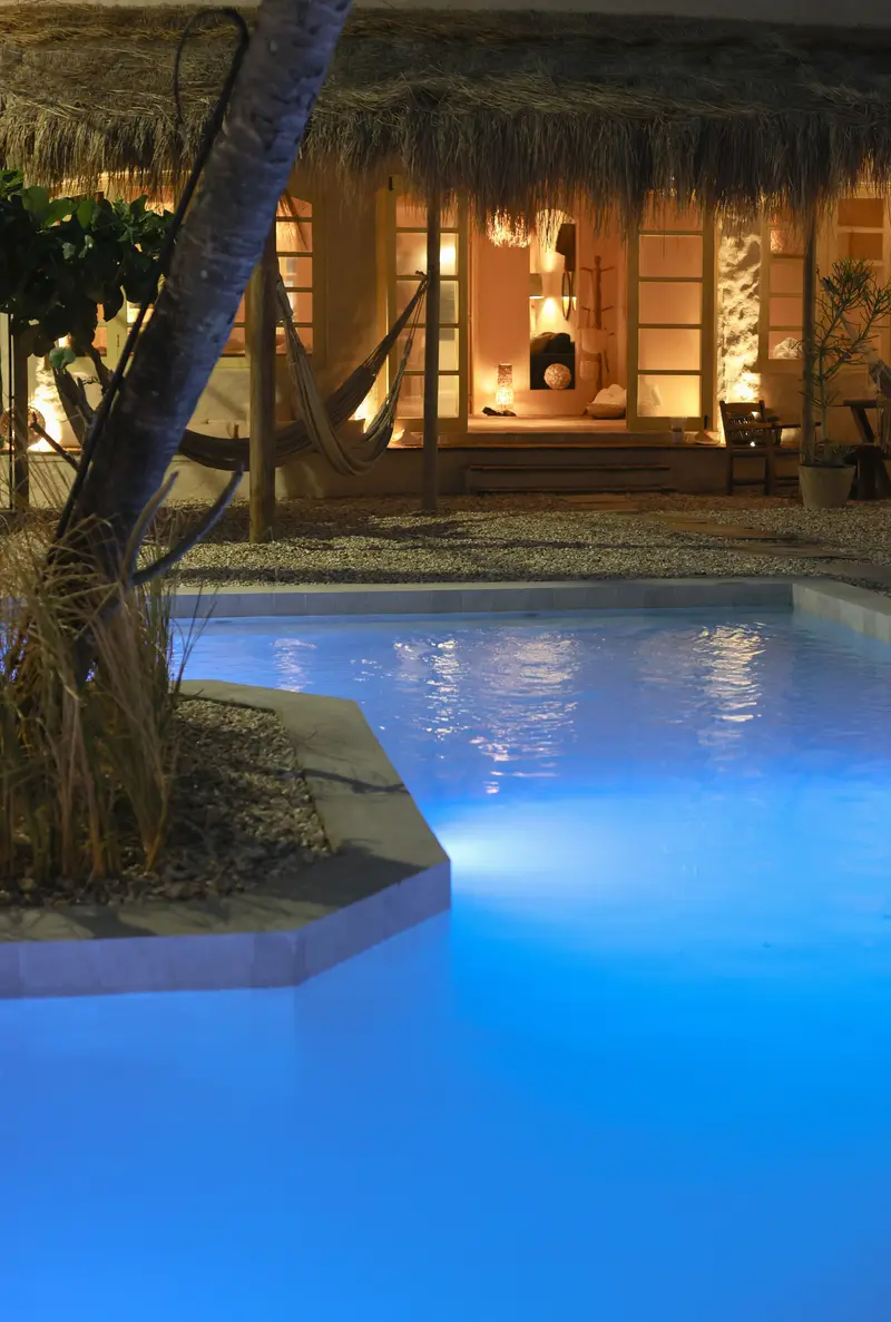 Piscina iluminada à noite, com a casa acesa ao fundo