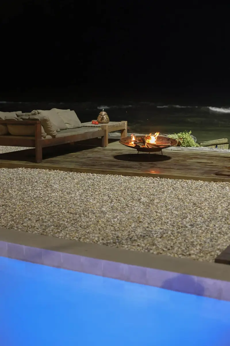 Deck à noite, com o fire pit aceso ao lado da piscina iluminada