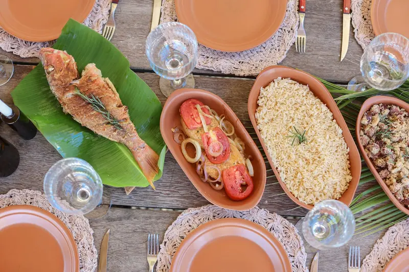 Mesa vista de cima com peixe, arroz e farofa em louça de barro